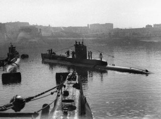 In the Malta submarine base within HMS TALBOT, three submarines: HMS UNITED (left) and HMS UNISON (right). Bows of HMS UNSEEN into the foreground.